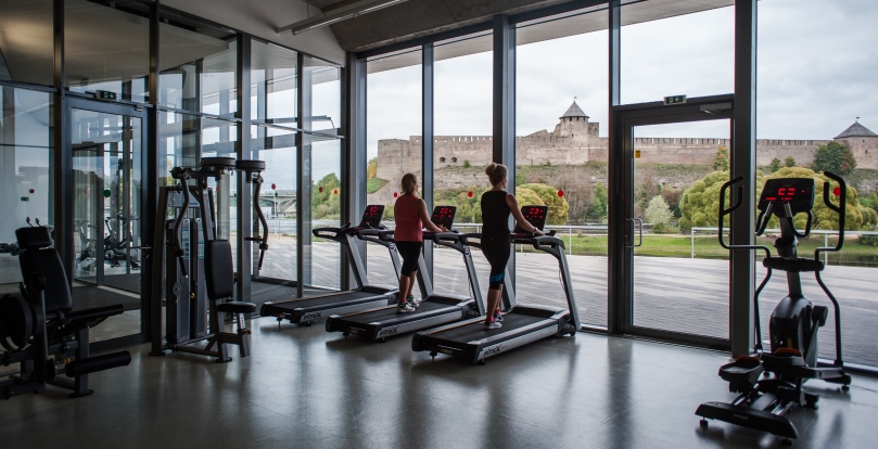 Why gym is good for businesses - Narva (Estonia), two women in a gym facing the Narva river observing the Russian fortress of Ivangorod – Alessandro Gandolfi/Parallelozero